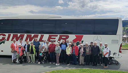 Gruppe älterer Menschen steht vor einem großen Reisebus mit der Aufschrift 'GIMMLER'
