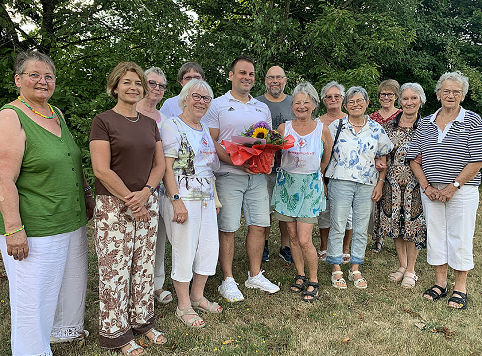 Gruppe von älteren und einem jüngeren Menschen im Freien, der jüngere Mann hält einen Blumenstrauß
