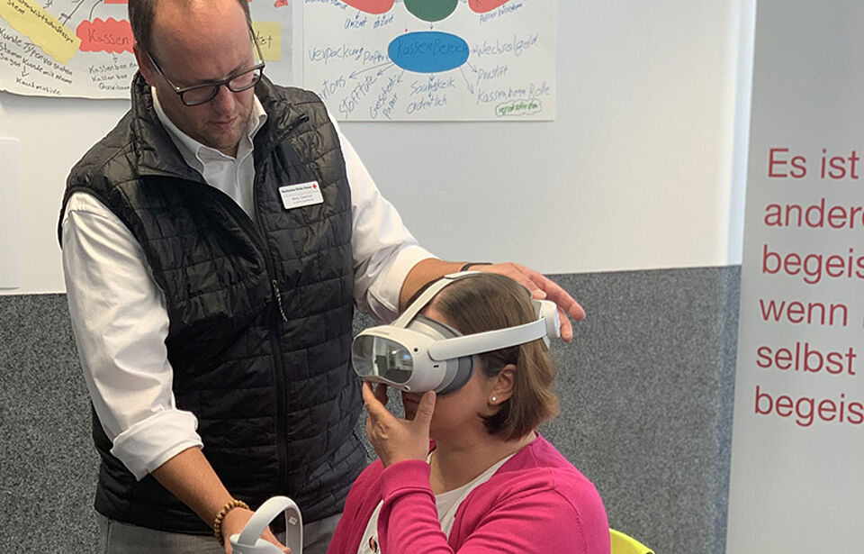 DRK-Mitarbeiter legt Frau eine VR-Brille an, die Frau hält einen Controller in der Hand